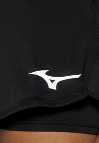 Ropa deportiva negra con textura suave, diseño ajustado y un acento del logo blanco de Mizuno. Detalles de costura visibles a lo largo de los bordes.