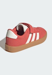 Červené semišové tenisky s bielymi doplnkami a tromi pruhmi. Majú suchý zips a svetlohnutú gumenú podrážku. Hladký povrch po celom obvode.