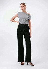 Top gris sin hombros combinado con jeans negros de pierna ancha de cintura alta, que cuentan con bolsillos frontales y costuras amarillas en contraste. Sandalias negras de tiras.