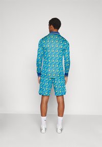 Langarmshirt und Shorts Set mit einem blauen Grundton und einem gelben Rautenmuster, ergänzt durch kontrastierende Bündchen und einen Bund.