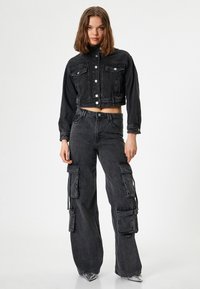 Svart denimjacka i cropped-modell med knappstängning och två bröstfickor, tillsammans med vida cargobyxor med flera sidofickor.