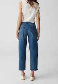 Blå denimjeans med hög midja, raka ben och beskuren längd. Subtil blekning med två bakfickor. Matchas med en ärmlös topp.