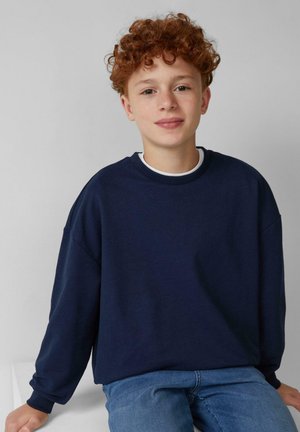 Navyblauwe sweatshirt met lange mouwen, ronde hals en een relaxte pasvorm. Draagt over een wit shirt, gecombineerd met blauwe jeans, tegen een lichte achtergrond.