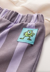 Tissu rayé gris et lavande avec un patch personnage de dessin animé vert sur une taille élastique. Texture lisse avec des couleurs vives.