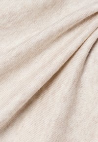 Hellbeige Stoff mit einer weichen Textur, der ein geripptes Muster und subtile Farbvariationen zeigt, was auf ein gemütliches, gestricktes Material hinweist.