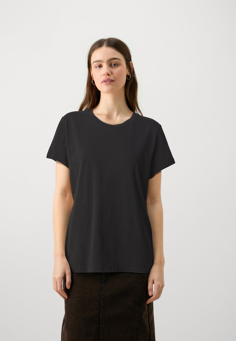 Camiseta corta negra de algodón, con un escote redondo y un corte relajado. Combinada con una falda oscura, de textura suave.