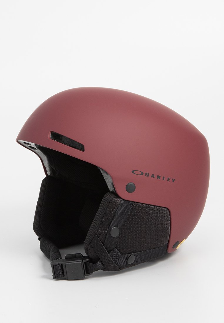 Casco rosso opaco con design arrotondato, imbottitura interna nera, cinturino regolabile e aperture per la ventilazione. Presenta il marchio "Oakley".