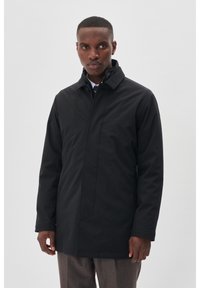 Cappotto impermeabile nero con colletto alto, taglio dritto e dettagli minimi. Texture liscia e tasche laterali funzionali.