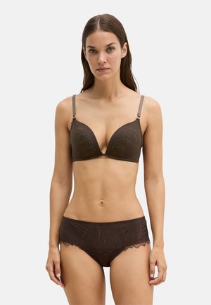 Woman wearing a matching brown bra and high-waisted panties with floral embroidery, standing against a plain light background.
