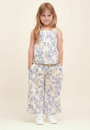 Lettet, blomstermønstret to-delt sæt i creme og blå. Ærmeløs top og bredbenede bukser med lommer, parret med hvide sneakers.