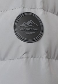Tessuto di giacca puffer grigia con una superficie testurizzata, caratterizzata da un patch rotondo in gomma nera con design montano e testo.