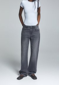 Jean gris à jambes larges avec une texture en denim lisse, doté de poches avant, d'une fermeture par bouton et d'une coupe décontractée. Associé à un haut blanc à manches courtes.