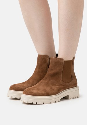 Stivali alla caviglia in suede marrone con finitura testurizzata, pannelli laterali elastici e una suola in gomma bianca spessa caratterizzata da un design battistrada.