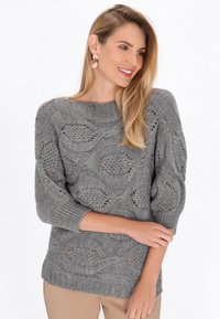 Grauer Strickpullover mit Wellenmuster und lockerem 3/4-Ärmeln. Rippkragen und Saum sorgen für zusätzliche Textur und Kontrast.