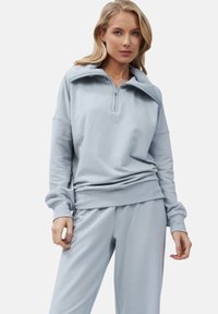 Lichtblauwe sweatshirt met een ritssluiting bij de kraag, ontspannen pasvorm, geribde mouwen en tailleband. Gecombineerd met bijpassende lichtblauwe sweatpants.