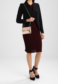 Svart blazer med sjalkrage, vinröd ribbad klänning och metallisk rosaguldig handväska på en silverkedja. Svarta klackskor med ankelrem.