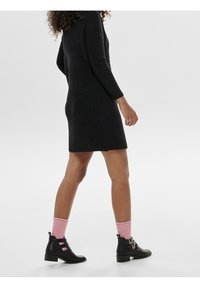 Abito nero lavorato a maglia con maniche lunghe, abbinato a stivali neri alla caviglia con doppie cinghie e calzini rosa a coste.