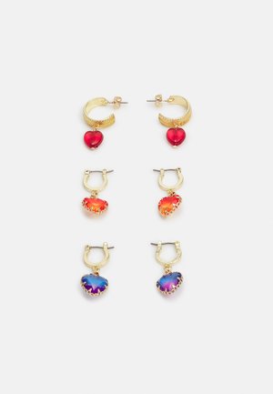 Brincos de argola dourada com pendentes em forma de coração coloridos: vermelho, laranja e azul de cima para baixo, apresentando diferentes texturas de gemas e contornos.