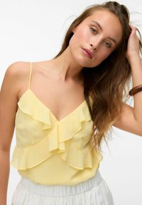 Geel, gelaagde ruffle blouse met dunne bandjes en een V-hals, gemaakt van lichte stof. Heeft een zachte textuur, gecombineerd met witte elastische taille shorts.