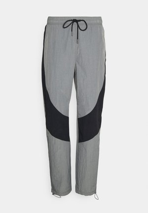 Lichtgrijze trainingsbroek met zwarte gebogen zijpanelen, elastische tailleband met zwarte trekkoorden en verstelbare koorden bij de pijpopeningen.