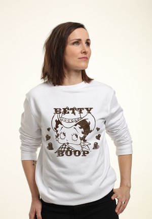 Biała bluza z brązowym nadrukiem Betty Boop w kapeluszu kowbojskim, otoczona motywami serduszek. Długie rękawy z ściągaczami.