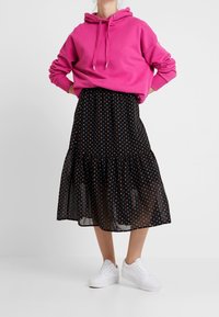 Rosa hoodie med dragsko, svart lagerkjol med färgglada hjärtmönster och vita sneakers. Tyget är mjukt och lätt.