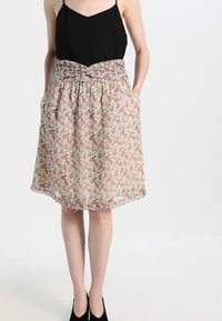 Falda floral con fondo beige, estampados en rosa y verde, cintura elástica y bolsillos. Tejido parcialmente transparente con una forma fluida.