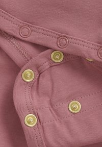 Rosa bomullstyg med synlig textur; har guldknappar för stängning. Sömdetaljer finns längs kanterna.