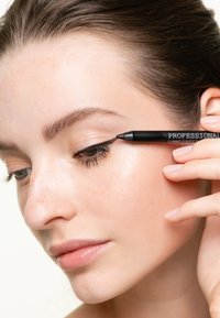 Svart eyelinerpenna märkt "PROFESSIONELL LÅNGVARIG" applicerad på ögonlocket. Ämnet har jämn hud med fräknar och naturlig läppfärg.