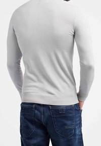 Maglione grigio chiaro a maglia con maniche lunghe, polsini e orlo a coste. Indossato con jeans in denim blu scuro con tasche posteriori e dettagli di cucitura.
