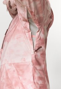 Hellrosa Kapuzenjacke mit einem Batikmuster, ausgestattet mit einem Netzfutter und seitlichen Reißverschlusstaschen. Glatte Textur mit detaillierter Näherei.