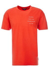 Heldere rode T-shirt met korte mouwen en witte tekst op de bovenste linkerzijde met de opmerking "The Original Scotch & Soda Amsterdam Couture Est. 1985."