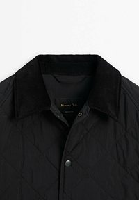 Musta tikattu takki, jossa on samettikaulus, painonapit ja sileä pinta. Sisällä näkyvä merkki.