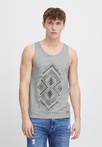 Grauer Tanktop mit einem geometrischen, tribal-inspirierten schwarzen Druck auf der Vorderseite; aus weichem Stoff; getragen mit blauen, verwaschenen Jeans.