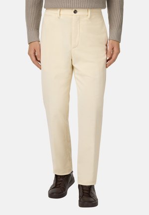 Pantalones de algodón beige con corte recto, con cierre de botón en la parte delantera y bolsillos laterales, combinados con zapatillas deportivas de color marrón oscuro.