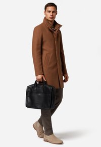 Brauner Wollmischmantel, schwarze Lederhandtasche, beigefarbene Wildlederstiefel, gerade geschnittene Hose. Saubere Linien und taillierte Passform, minimalistisch im Design.