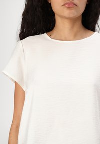 T-shirt bianco a maniche corte realizzato in un tessuto morbido e strutturato, con scollatura rotonda e un fit rilassato, caratterizzato da leggere pieghe.