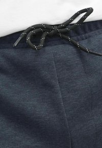 Marineblauwe joggers met een geribbelde textuur en een zwarte trekkoord. Het trekkoord heeft witte accenten en is knoop gedaan in de taille.