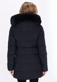 Marineblå dunjakke med faux fur krave, prydet med vandret quiltet design, lange ærmer og en mellemlang pasform.