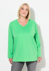 Langmouwen V-hals shirt in felgroen, gemaakt van gladde stof met een relaxte pasvorm, gecombineerd met grijze jeans. Eenvoudig ontwerp zonder patronen.