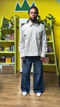 Geruit overhemd met knopen in wit en lichtblauw, gecombineerd met wijde blauwe jeans. Witte sneakers maken de outfit compleet. Groene achtergrondaccenten.