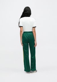 Zielone spodnie sportowe z żółtymi paskami po bokach, elastyczny pas; połączone z białym t-shirtem z czarną lamówką. Widok od tyłu, widoczne włosy.