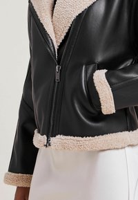 Czarna skórzana kurtka z beżowym kołnierzem i mankietami z owczej wełny. Posiada zamek błyskawiczny z przodu, boczne kieszenie oraz gładką fakturę.