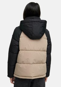 Pufferjack met een capuchon, met een zwarte bovenkant en een beige onderkant. Zachte, gewatteerde textuur met horizontale naden.