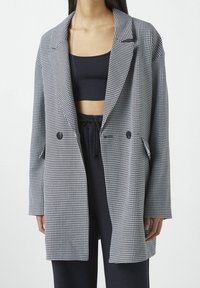 Blazer a cuadros en blanco y negro, con un corte holgado, solapas con muesca, cierre de doble botón y bolsillos laterales. Textura de tela suave.