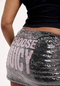 Ezüst flitteres miniszoknya, világos rózsaszín "CHOOSE JUICY" felirattal. Simogató textúrájú, testhezálló kialakítású, fényt tükröző.