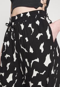 Pantalon noir et blanc à motifs avec une taille élastique, poches latérales et une coupe décontractée, mettant en avant des formes abstraites sur un tissu texturé.