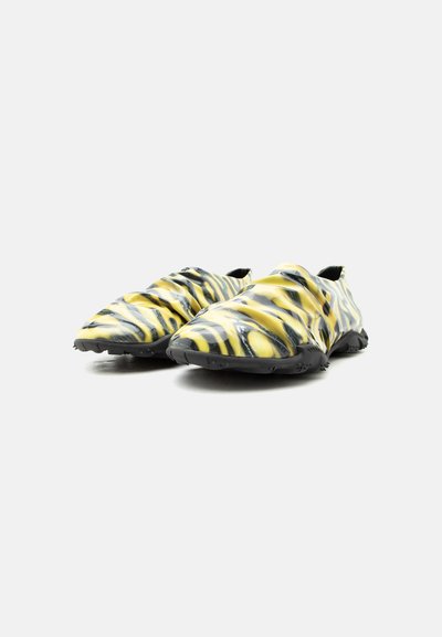 Κίτρινα και μαύρα παπούτσια τύπου slip-on με ρίγες τίγρης, υφή στη σόλα από καουτσούκ και κομψό, ευέλικτο σχεδιασμό, εμφανιζόμενα δίπλα δίπλα σε λευκό φόντο.