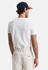 Hvid t-shirt med korte ærmer parret med lysebeige bukser, der har en tekstureret stof og en klassisk pasform. Simpelt, rent design.