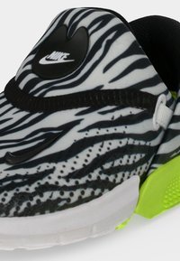 Κοντινή λήψη παπουτσιού Nike με ασπρόμαυρες ρίγες ζέβρας, μαύρο σήμα, άσπρη σόλα και λεπτομέρεια τακουνιού σε νέον πράσινο.